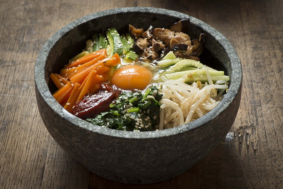 Traditional dolsot bibimbap in a black stone bowl with assorted vegetables, rice and egg