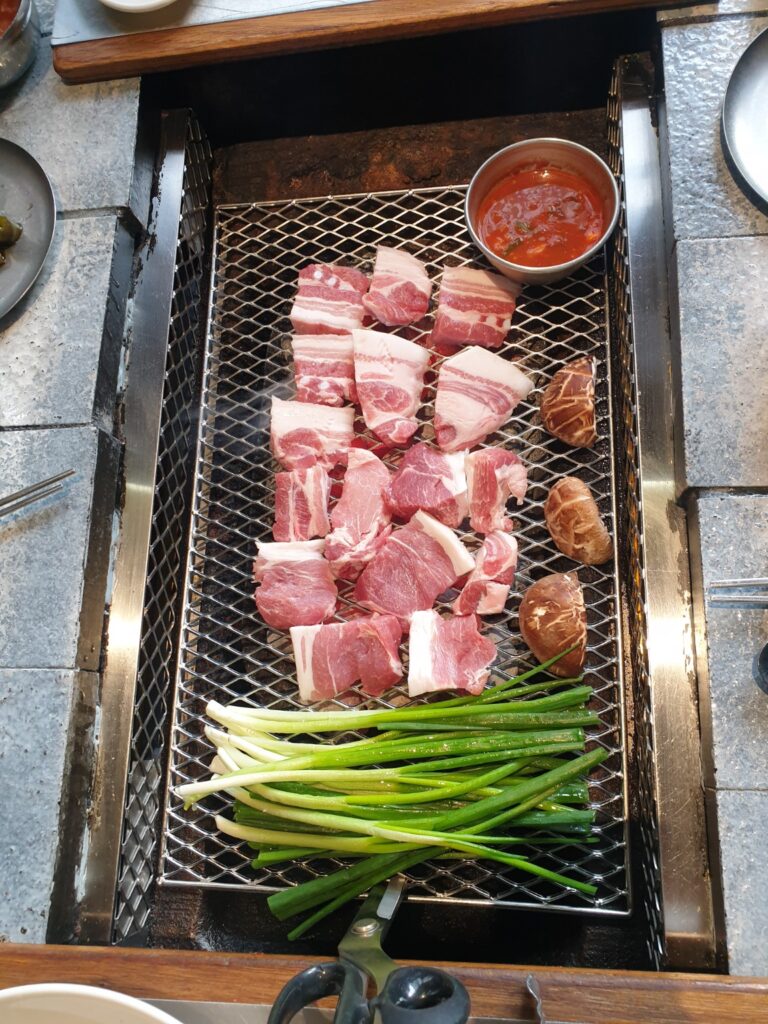 Samgyeopsal (Korean pork belly) with green onions and mushrooms on a Korean BBQ grill