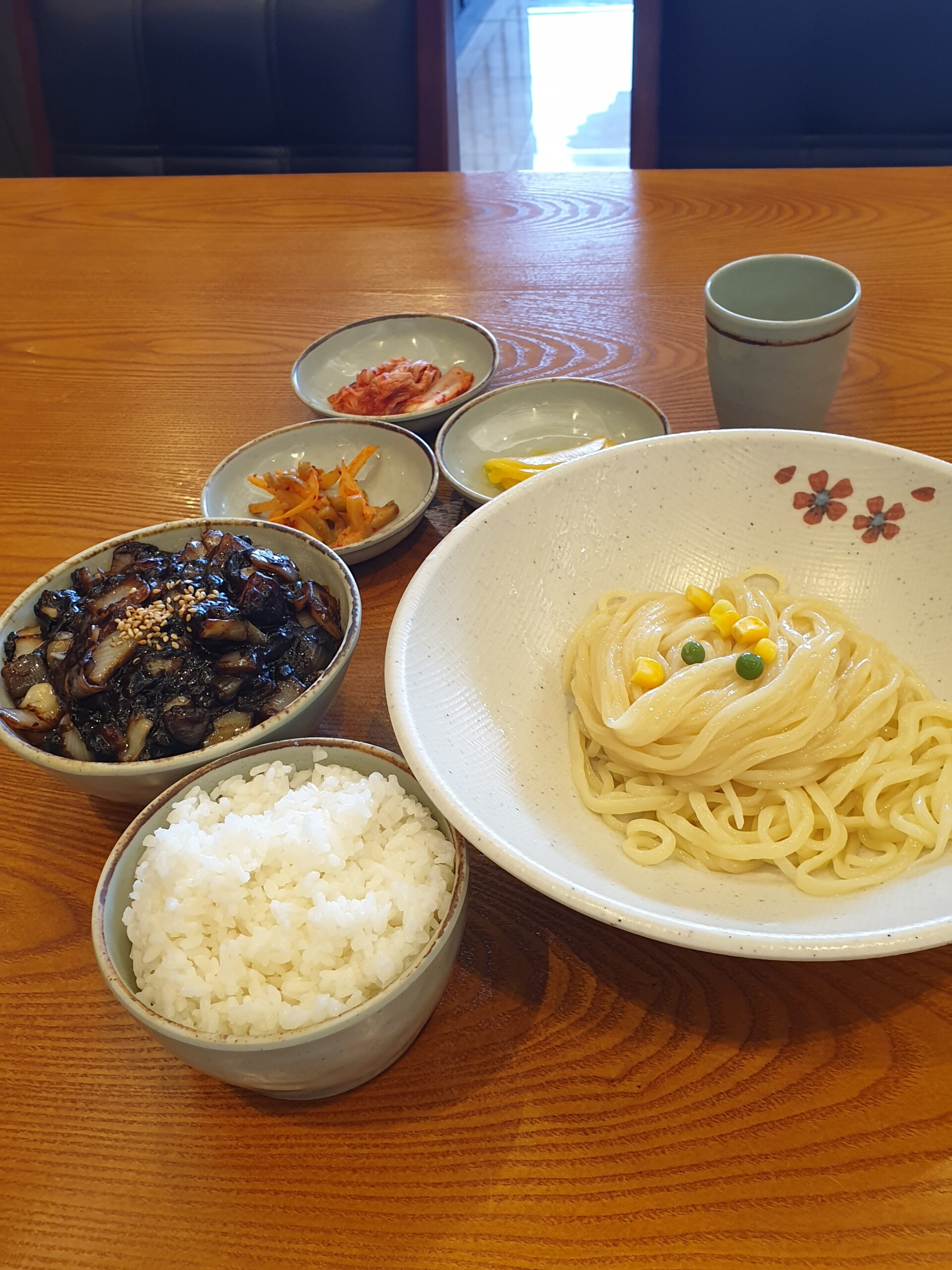 Ganjjajang noodles served separately from a bowl of thick black bean sauce, with a small bowl of steamed white rice visible at the lower left