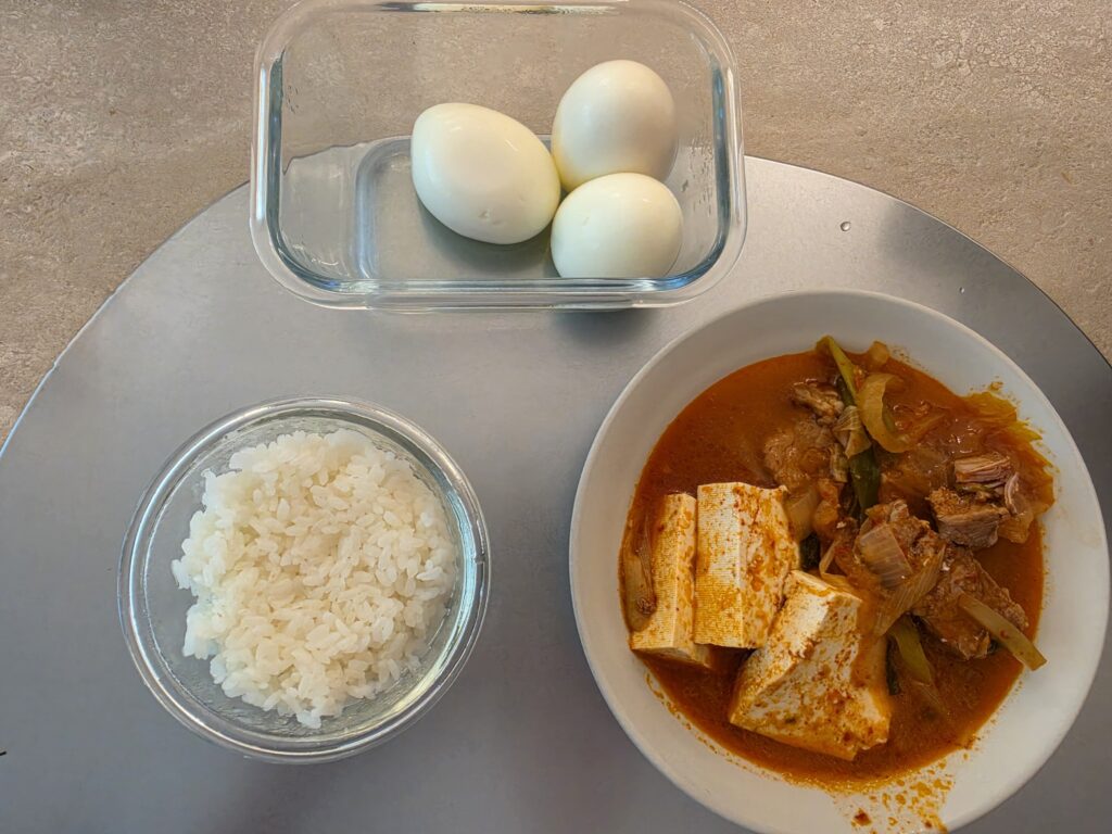 Korean homemade meal with rice on the left, kimchi jjigae on the right and boiled eggs