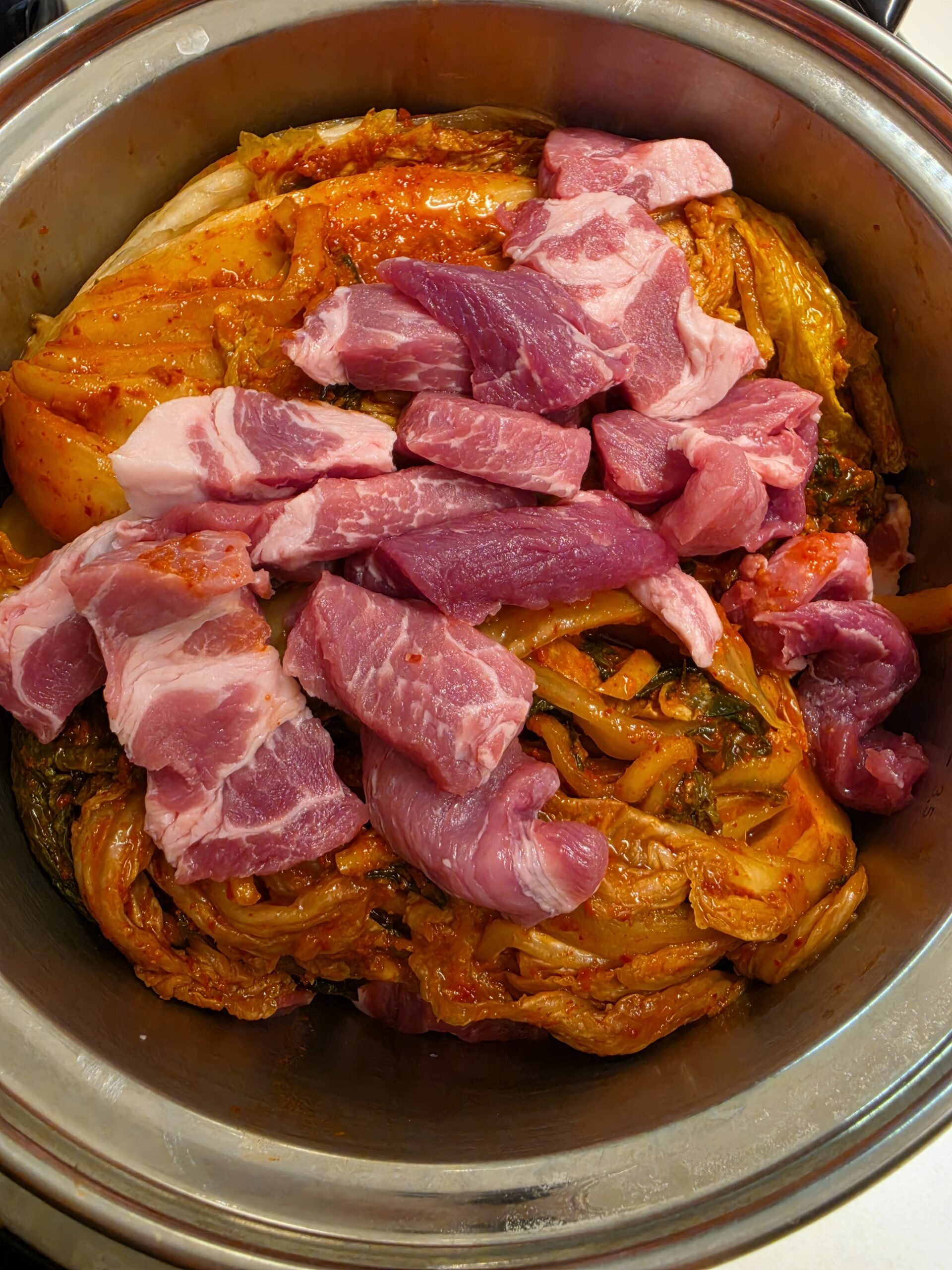 Raw pork and fermented kimchi in a pot before cooking kimchi jjigae