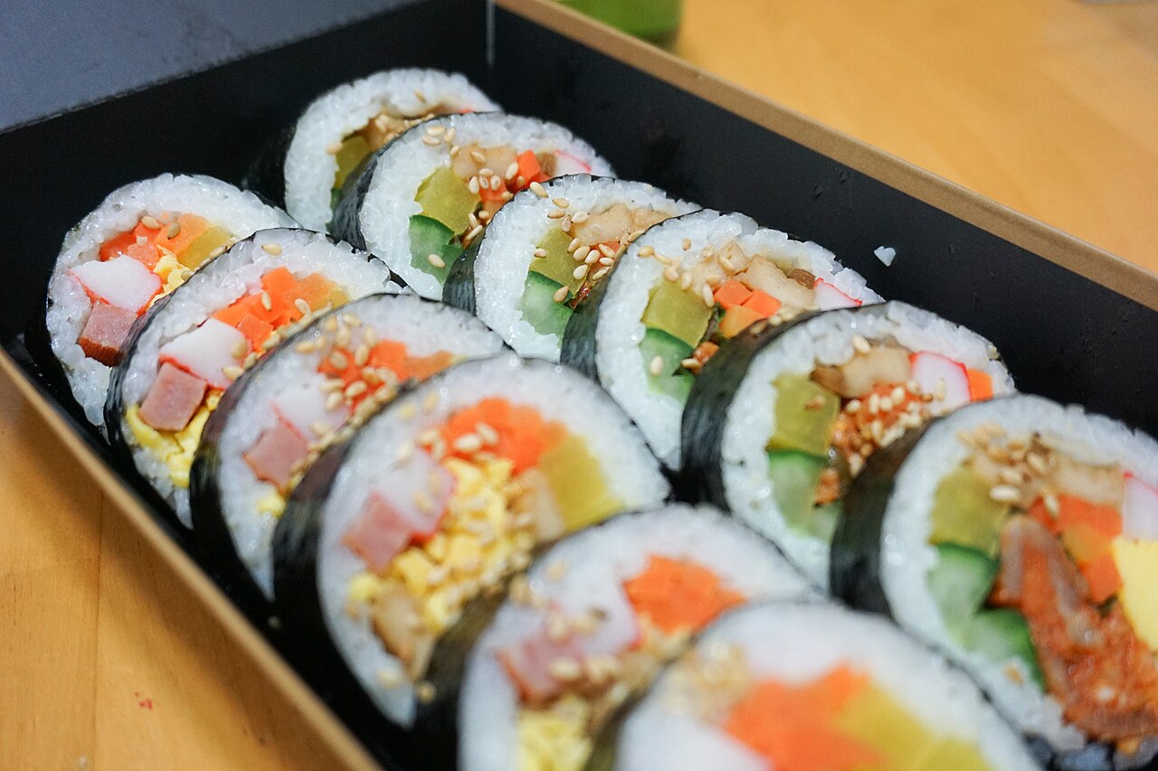 Sliced Korean vegetable gimbap with pickled radish, carrot, egg and ham in a lunchbox