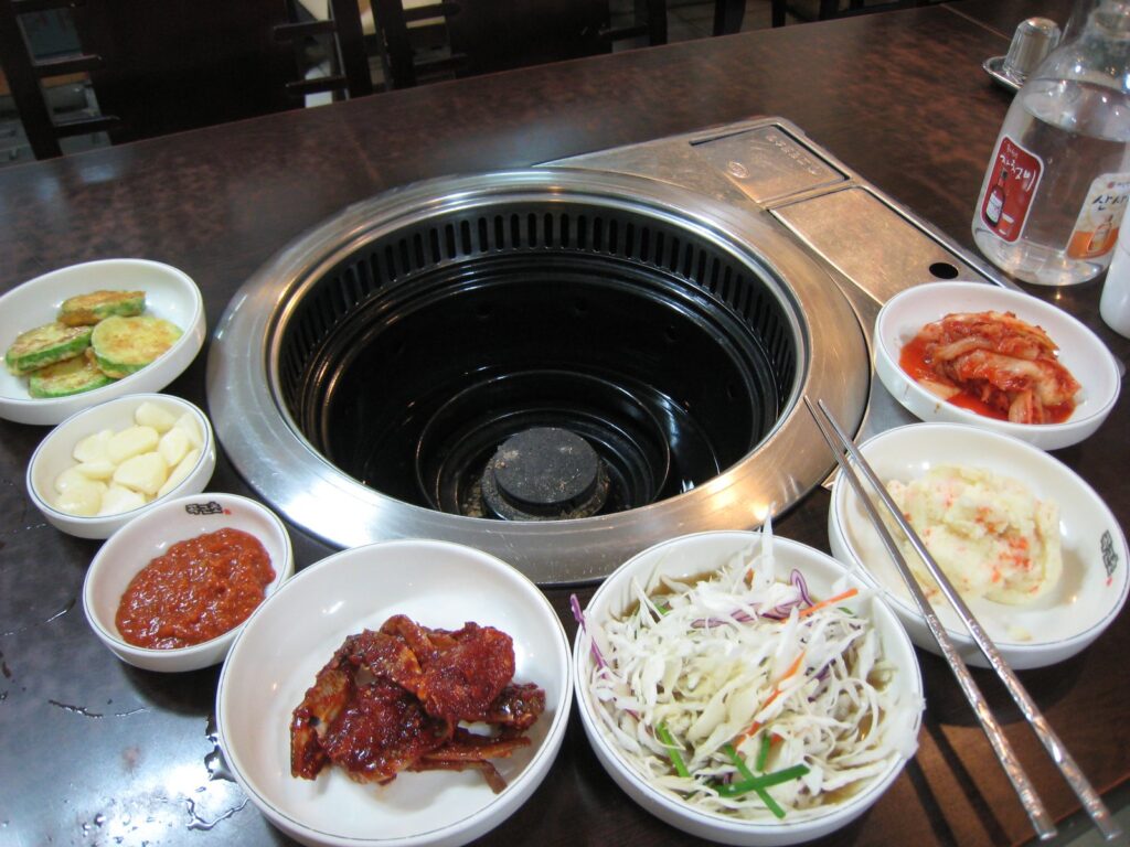A restaurant table in Seoul with a built-in grill surrounded by small plates of banchan, kimchi, and salad.